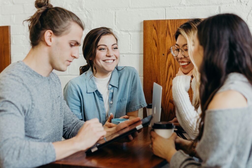 A group of young professionals collaborating at a café, smiling and discussing ideas on a tablet and laptop — a perfect example of teamwork and engagement powered by AI powered marketing.