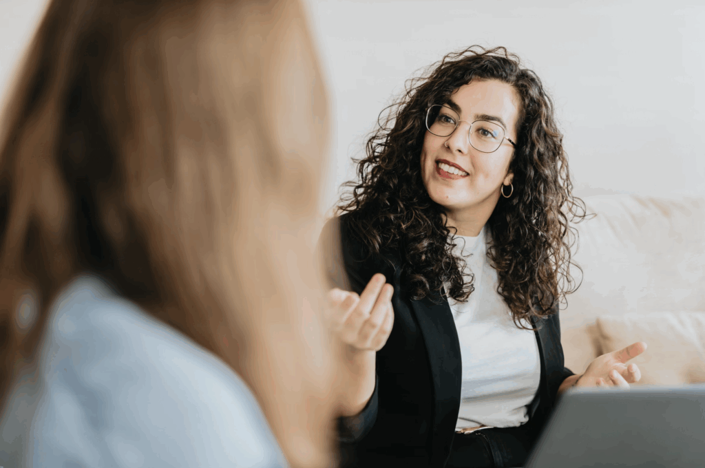 Smiling HR professional having a conversation with a colleague while working on a laptop, illustrating how AI for Human Resources enhances employee engagement and communication.
