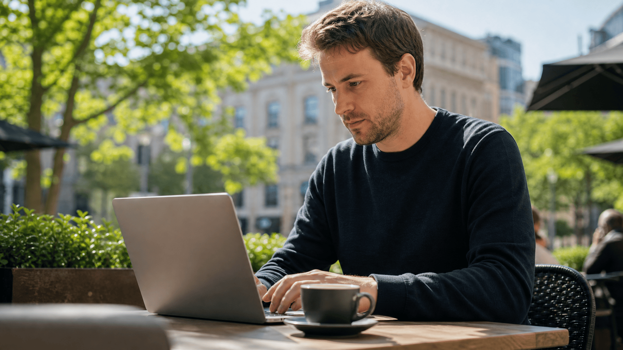 Person working on a laptop at a sunny cafe terrace
