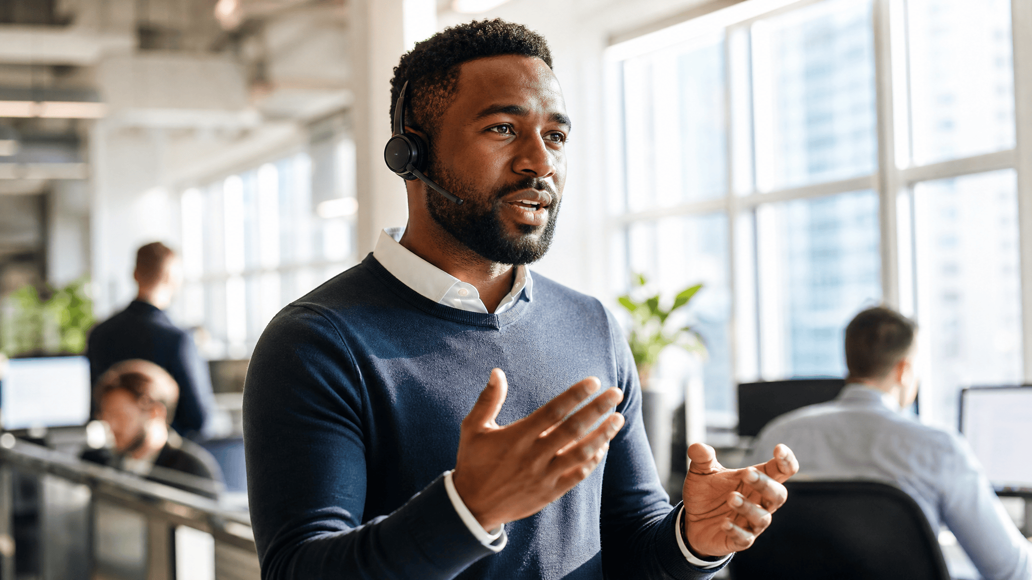 Sales rep with a headset gesturing on a call in a bright office
