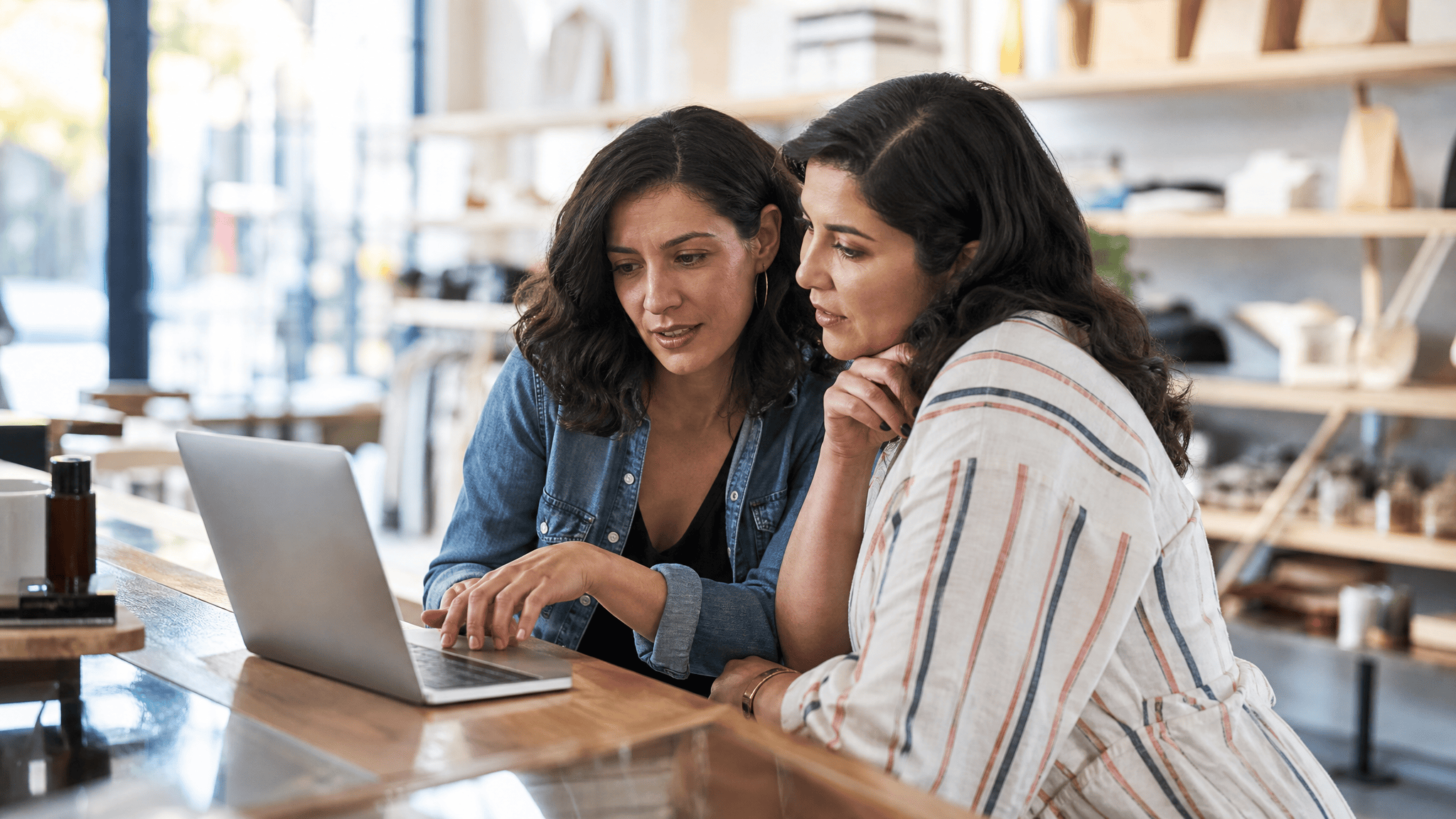Latina small business owner and colleague working on a laptop in a shop