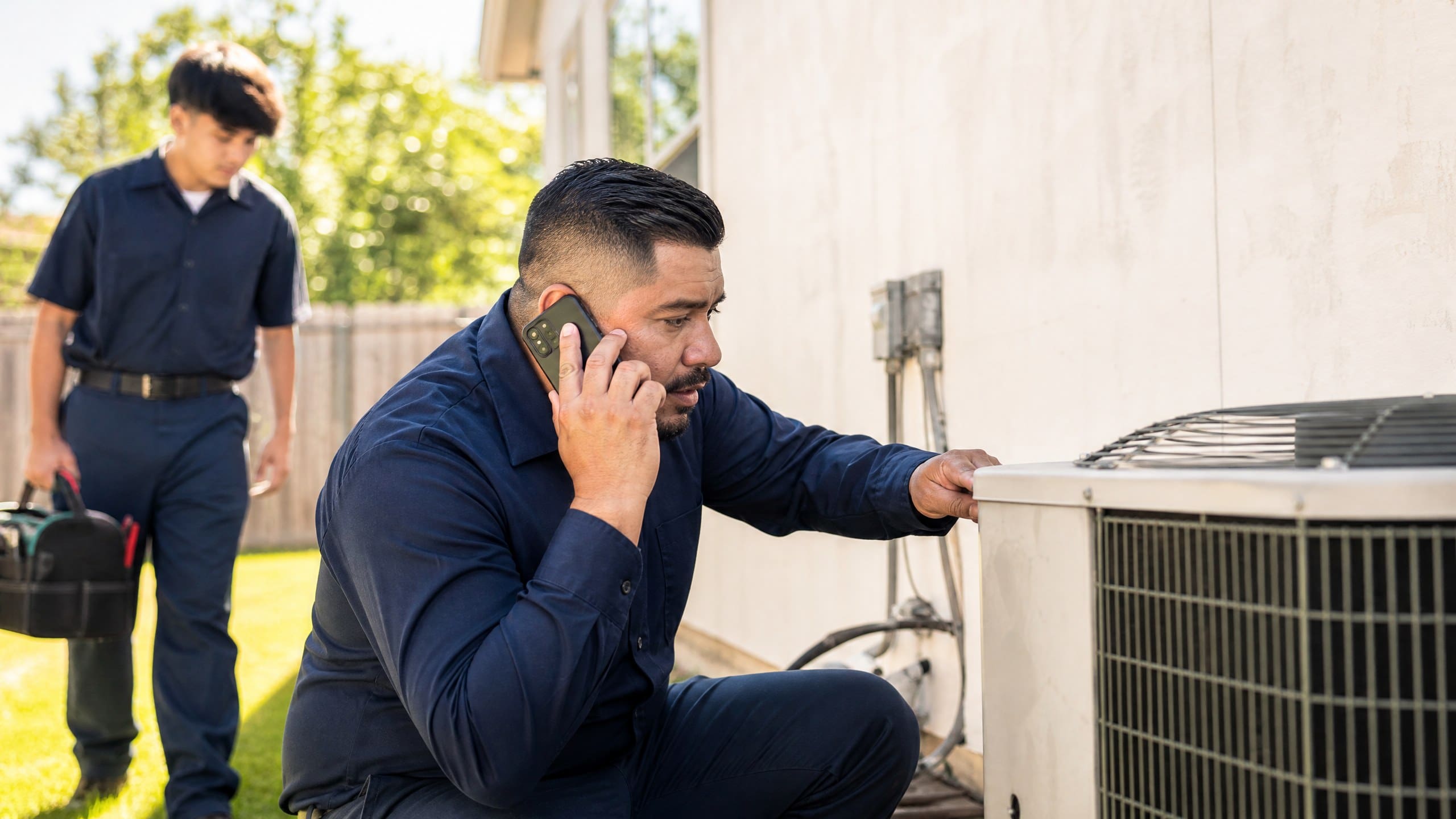 HVAC technician on a phone call next to an outdoor air conditioning unit
